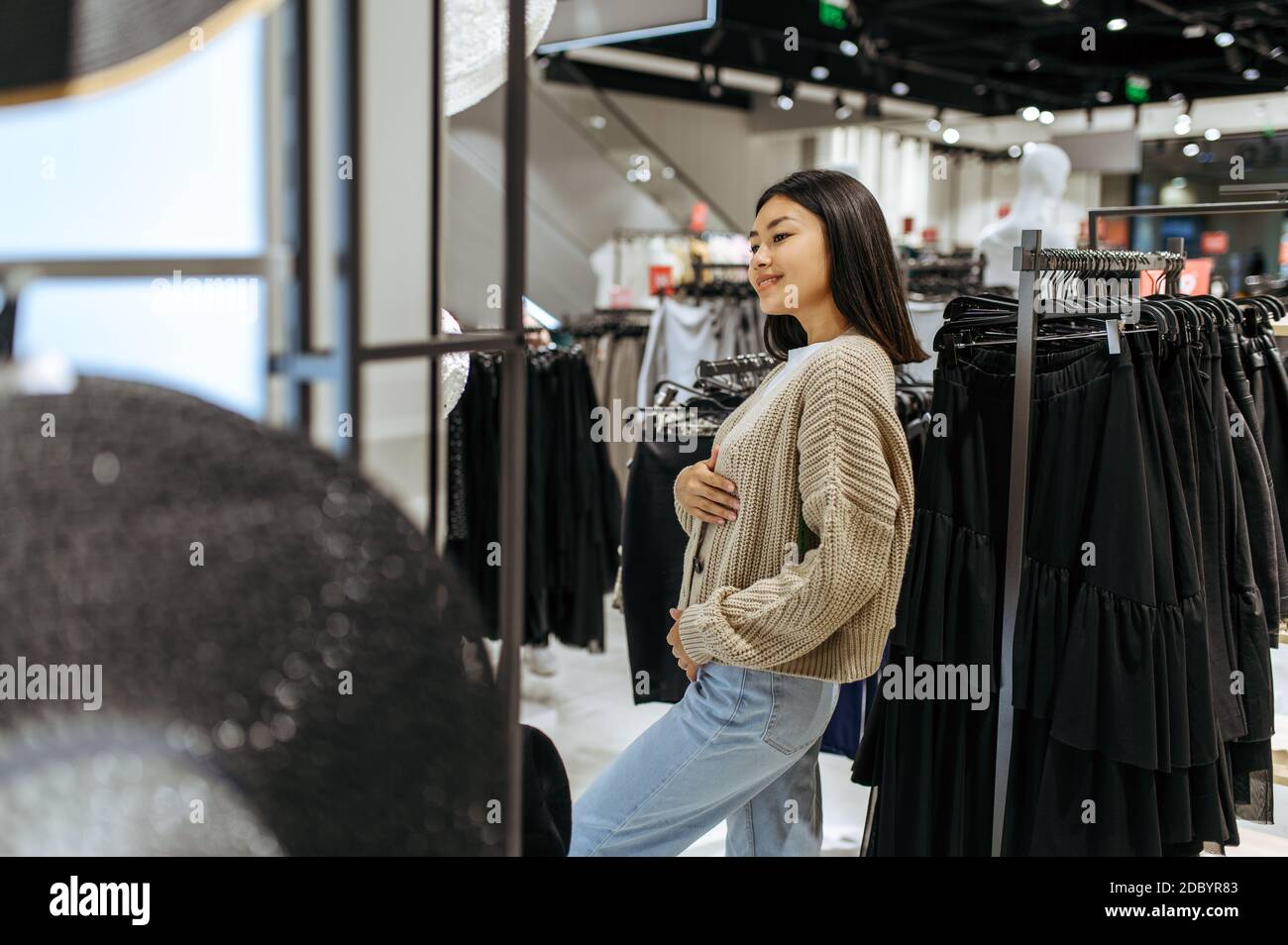 Mujer joven intentando en el cárdigan en la tienda de ropa. Mujer persona  de compras en boutique de moda, shopaholic, comprador buscando ropa  Fotografía de stock - Alamy