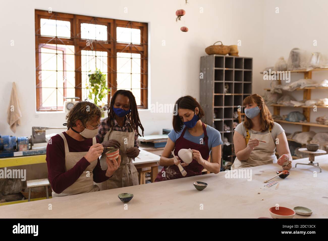 Grupo multiétnico de alfareros en máscaras de cara que trabajan en cerámica estudio Foto de stock