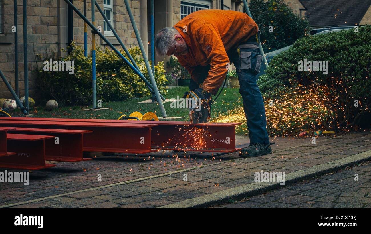 Trabajador con ropa protectora cortando a través de acero RSJ con una sierra de metal circular creando chispas en un sitio de construcción doméstica, Inglaterra Foto de stock
