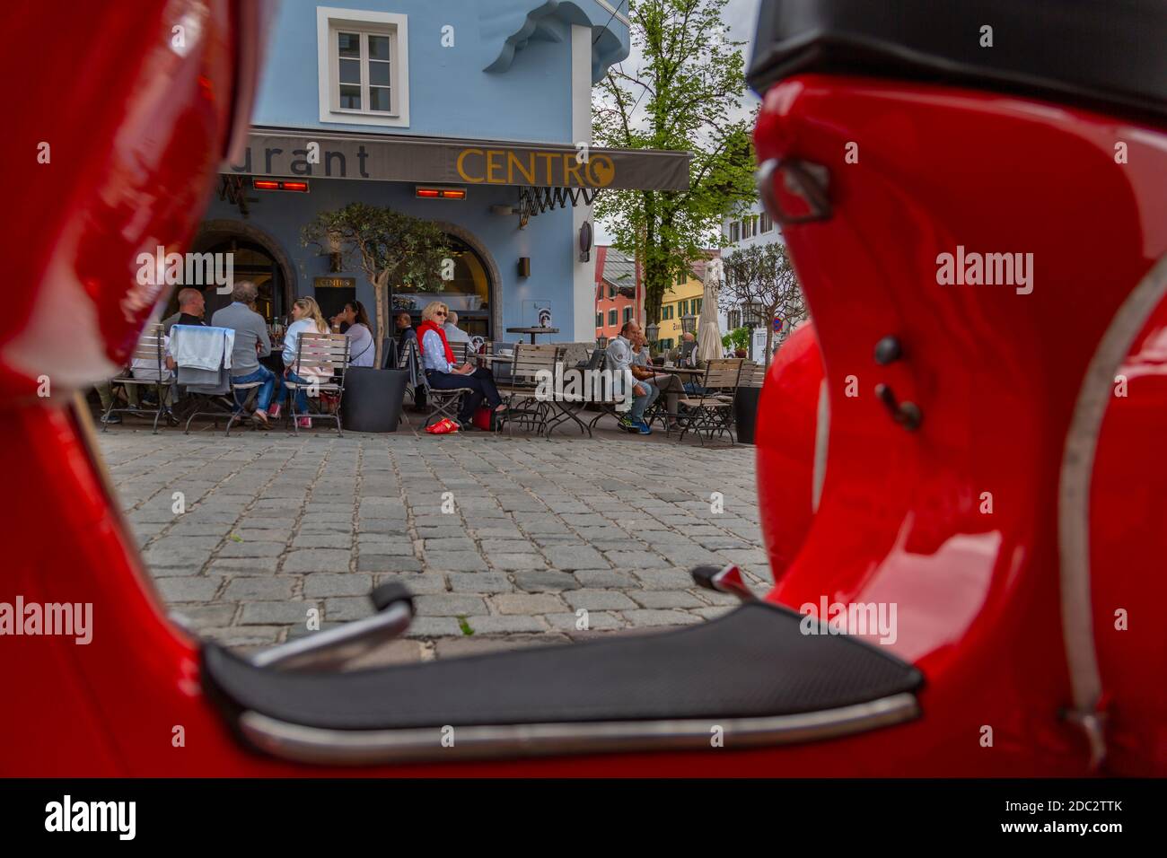 Vista de los visitantes disfrutando de bebidas fuera del café enmarcado por una scooter roja en Vorderstadt, Kitzbuhel, Región del Tirol austriaco, Austria, Europa Foto de stock