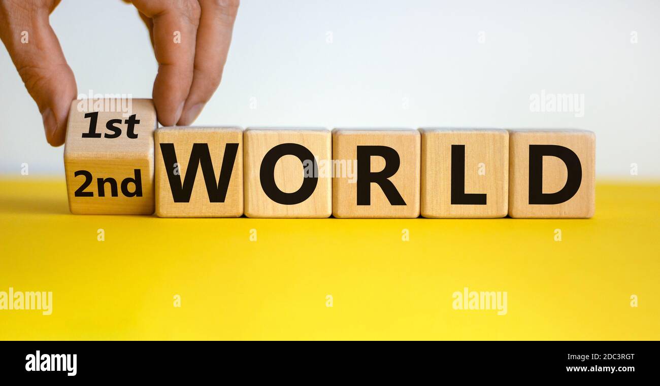 La mano masculina voltea un cubo de madera y cambia la inscripción "2do mundo" a "1er mundo". Hermosa mesa amarilla, fondo blanco, espacio de copia. Negocio c Foto de stock