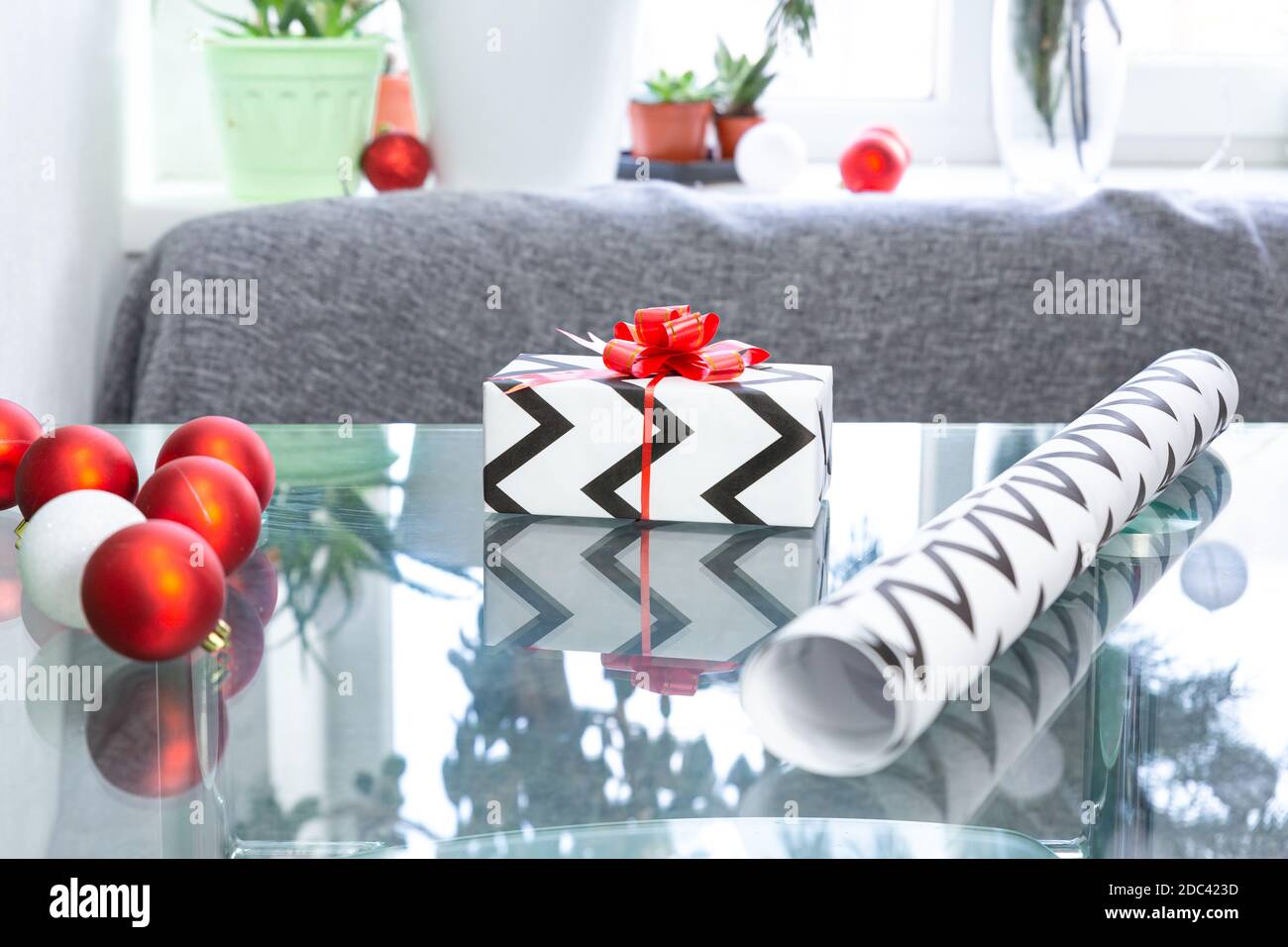 Regalo de Navidad, papel para envolver, bolas de Navidad en una mesa de  vidrio contra el fondo de una ventana con plantas interiores en macetas.  Año Nuevo, Navidad, invierno Fotografía de stock -