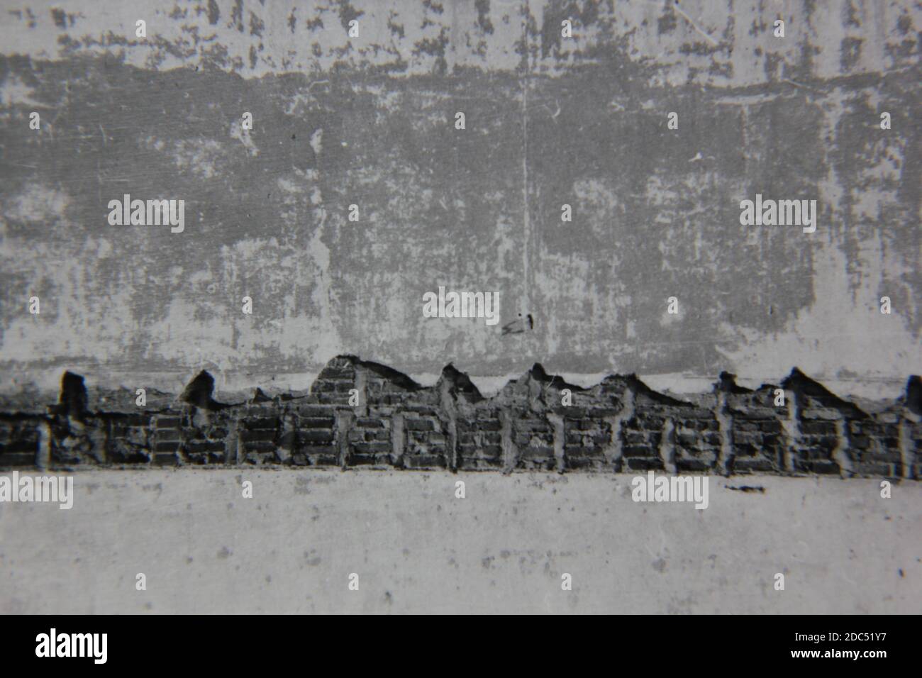 Fotografía en blanco y negro de la época de los años 70 de una pared de yeso desmoronada con una estructura de ladrillo. Foto de stock