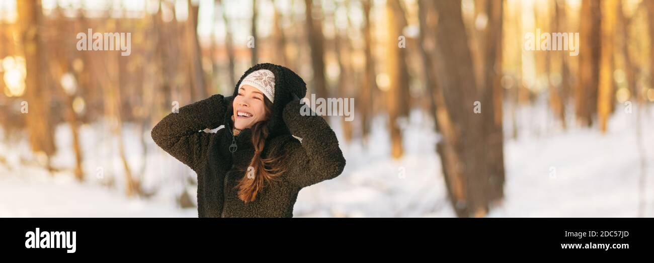 Invierno clima frío mujer proteger oídos sosteniendo sombrero caliente sobre orejeras bosque fondo banner panorama. Protección contra congelación ropa exterior niña asiática Foto de stock