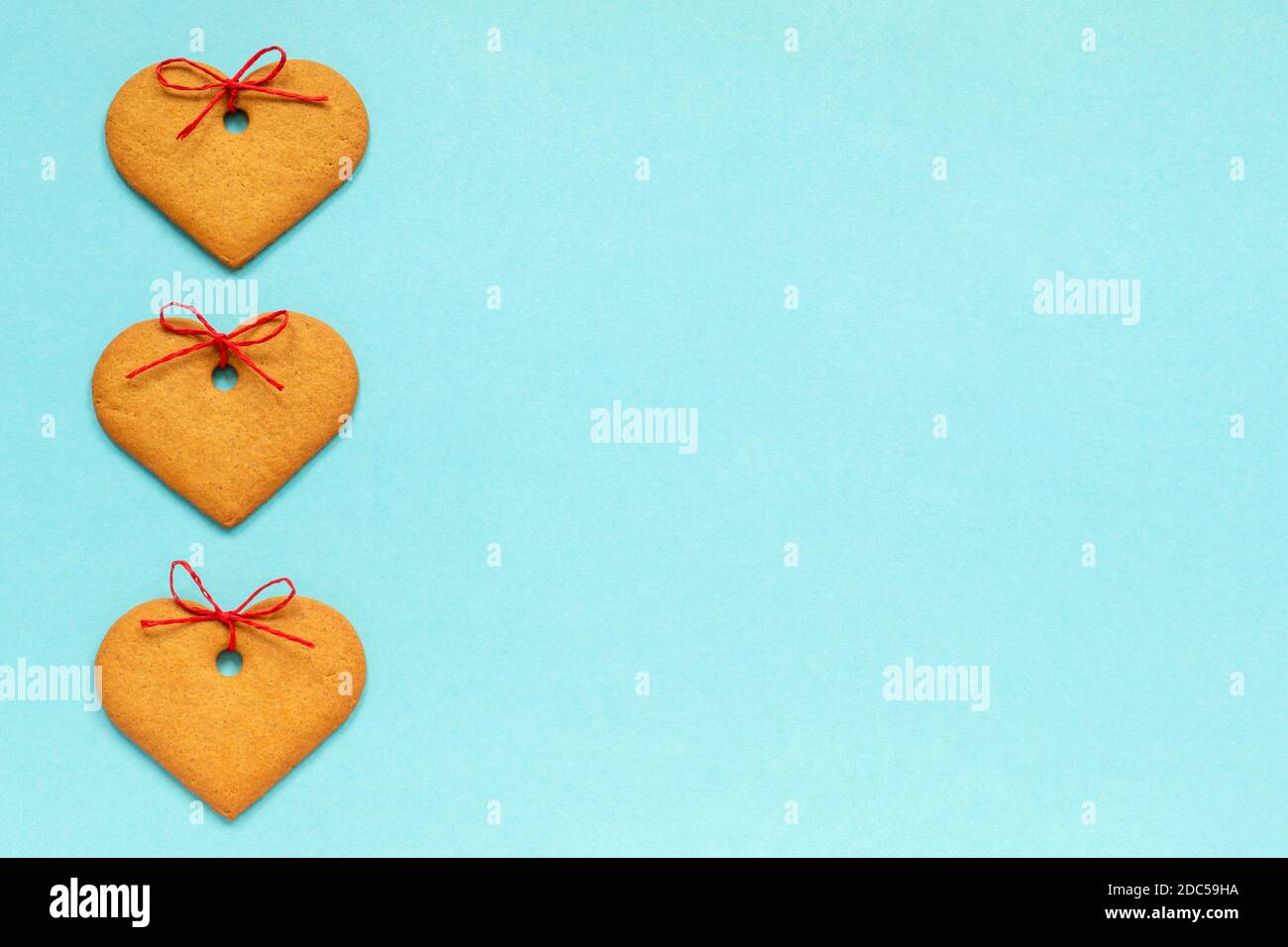 Galletas de jengibre en forma de corazón decoradas con un arco dispuesto en una fila vertical a la izquierda sobre un fondo azul. Vista superior Copiar espacio tarjeta de San Valentín. Foto de stock