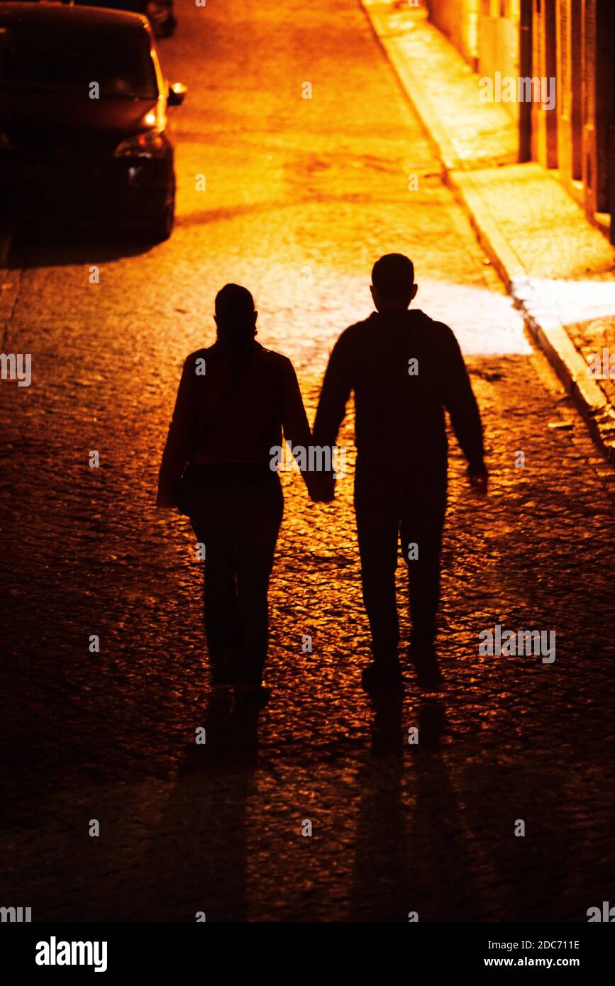 Silueta de una pareja con las manos caminando sobre un adoquín calle por la  noche Fotografía de stock - Alamy