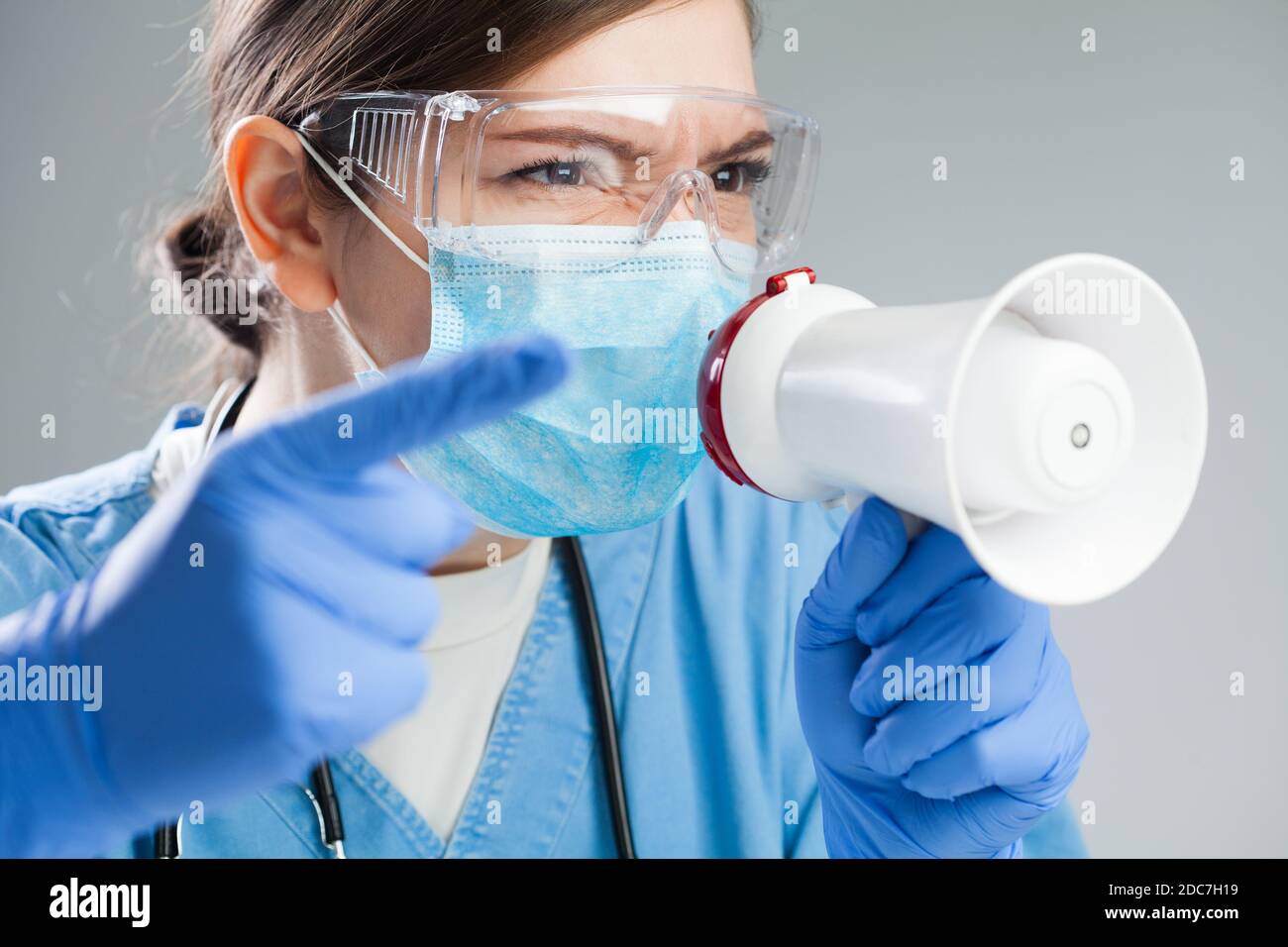 Doctor enojado en uniforme azul gritando órdenes y órdenes sobre megáfono, personal de manejo médico y pacientes en situación de cuarentena o emergencia,Corona Foto de stock