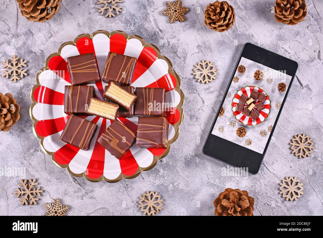 Concepto para fotografía de alimentos con pralinés de pastel de invierno con capas alemanas Llamado 'Baumkuchen' en la placa junto al teléfono móvil con foto tomado de comida Foto de stock