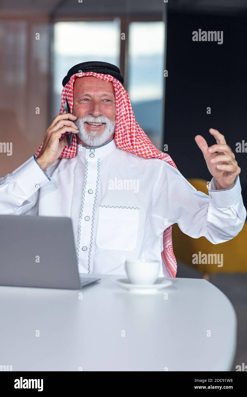 Hombre de negocios árabe ordenador portátil en la oficina moderna utilizando el teléfono Foto de stock