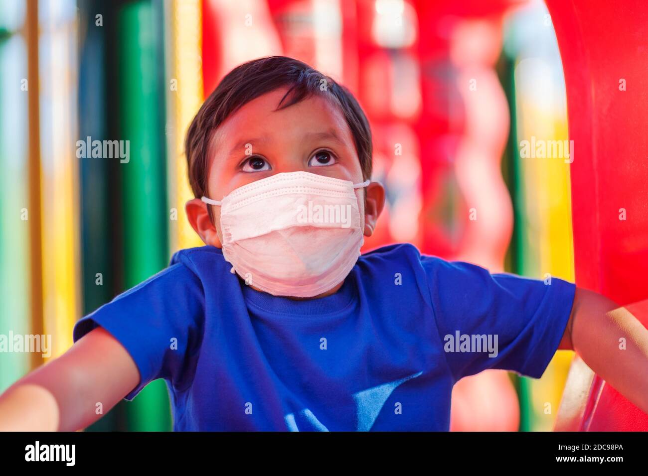 Niño que sube a un patio de juegos para niños mientras lleva una máscara para protegerse contra los virus en lugares públicos. Foto de stock