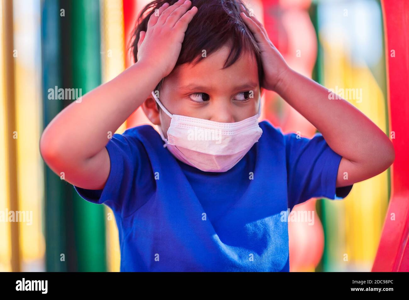 Niño latino usando una máscara durante las restricciones covid-19, mientras juega en un patio público. Foto de stock