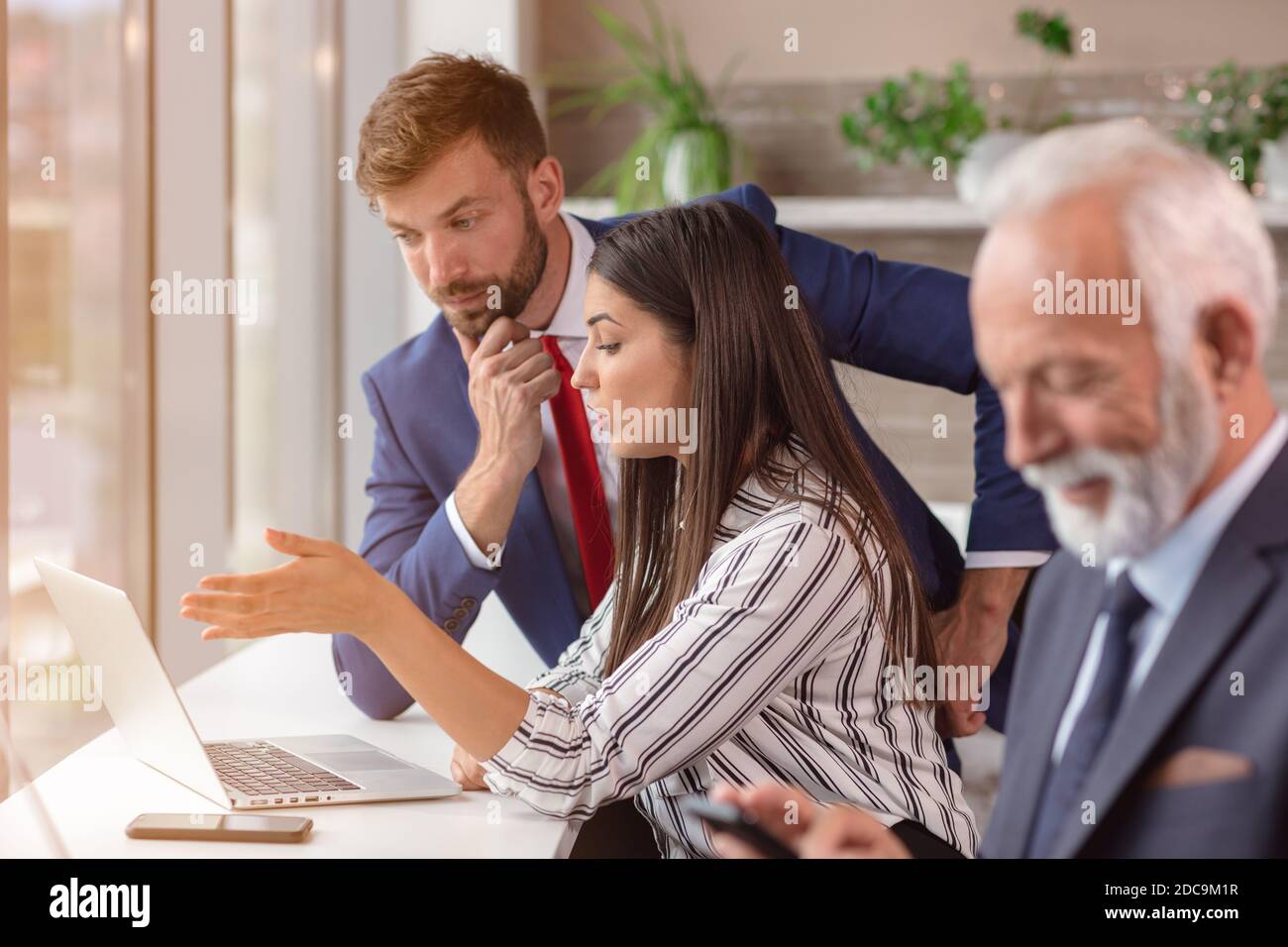 Retrato de un grupo de compañeros corporativos diversos que están a continuación a la ventana en una mesa en una oficina moderna y luminosa Foto de stock