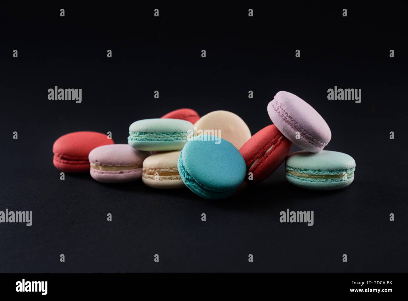 Primer plano de deliciosas galletas de postre en la mesa, aisladas sobre fondo negro. Vista frontal de coloridos macarrones dulces variados con diferentes sabores. Concepto de pastelería dulce. Foto de stock