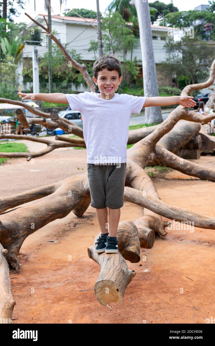 Niño de 6 años montando en una scooter y subiendo un tronco de árbol en la hermosa plaza Horácio Sabino. Foto de stock