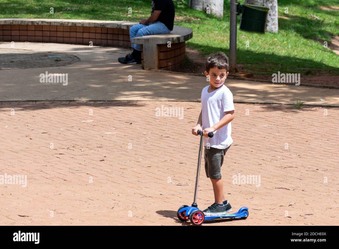 Niño de 6 años montando en una scooter y subiendo un tronco de árbol en la hermosa plaza Horácio Sabino. Foto de stock