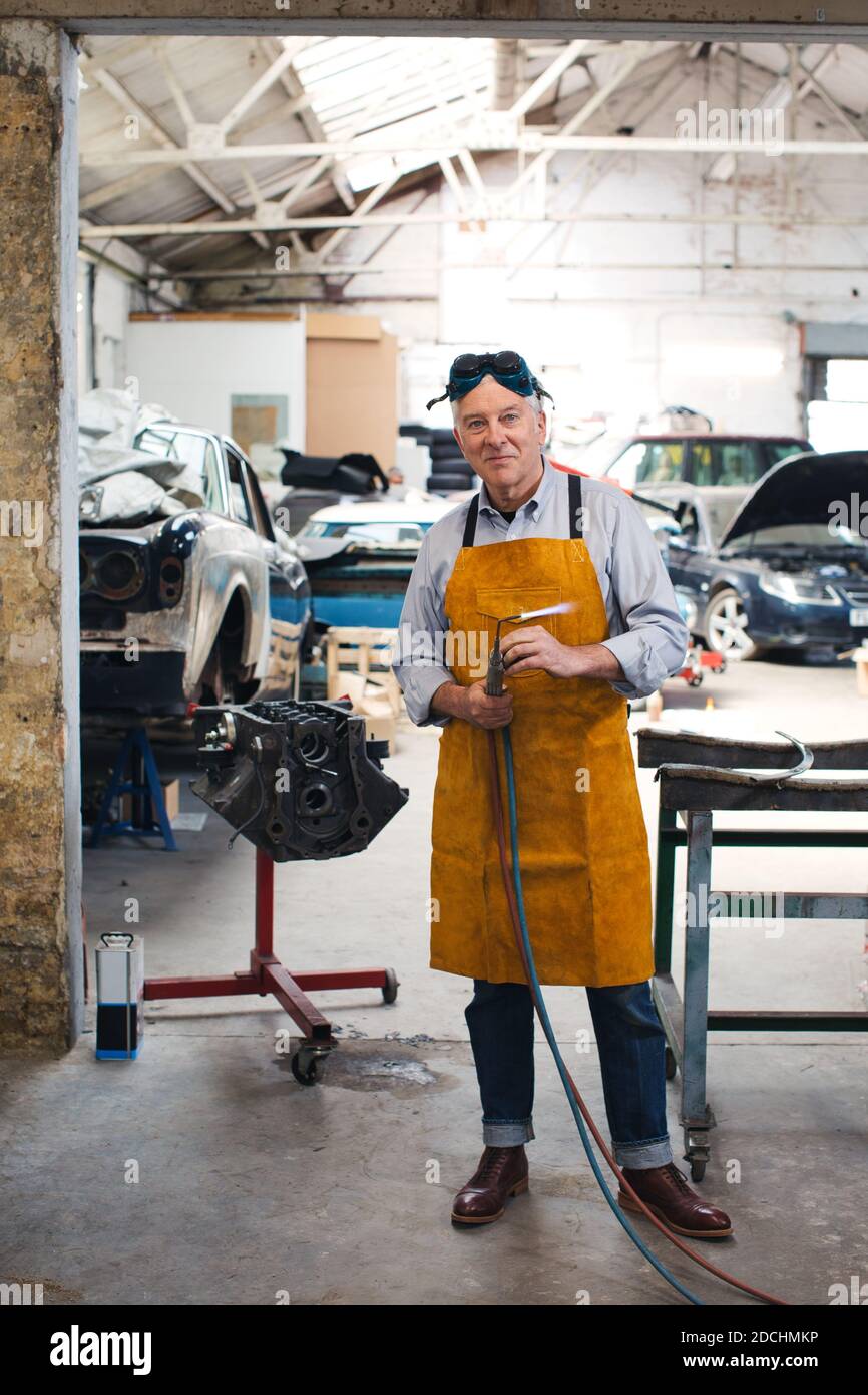 Mecánico que sostiene la antorcha de soldadura en un taller de garaje. Foto de stock