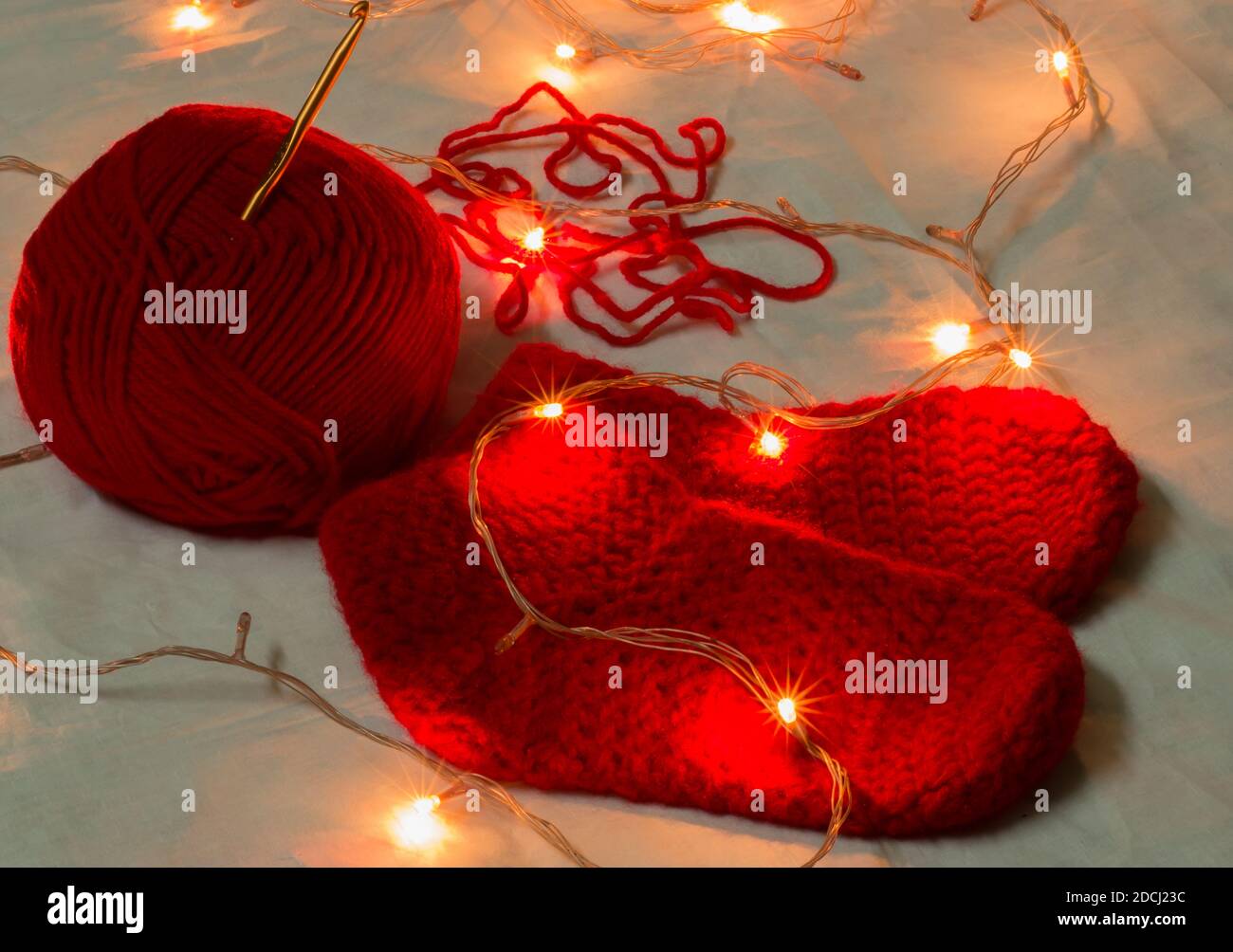 Calcetines de Navidad de lana de color rojo hechos a mano, aguja de chrochet y bola de lana iluminada con luces de Navidad en miniatura. Copiar fondo de espacio Foto de stock