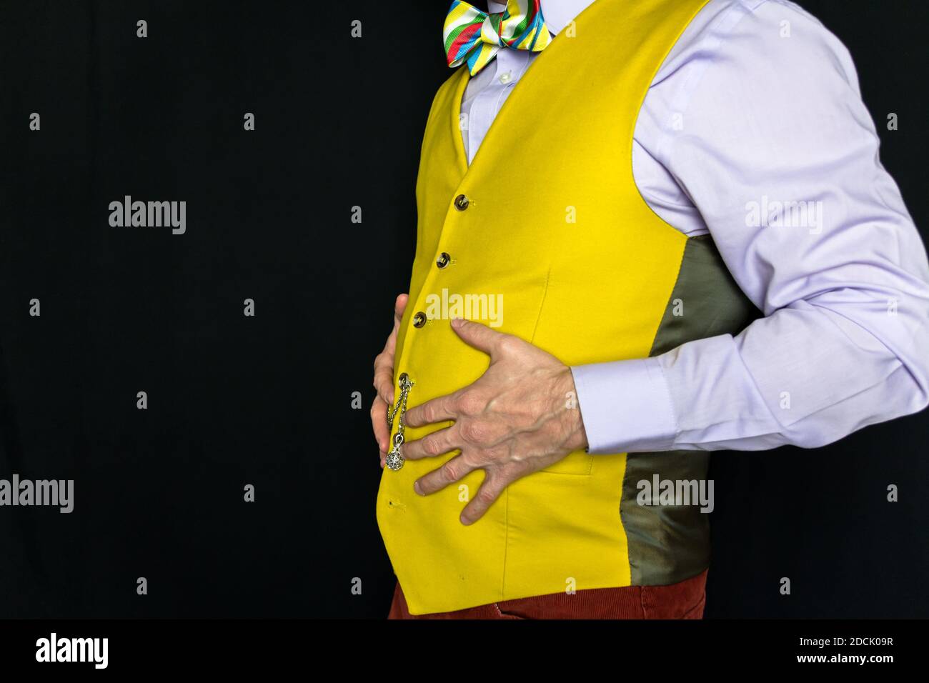 Retrato del hombre en chaleco amarillo brillante con las manos en su vientre. Concepto de comer en exceso. Copiar espacio para Gluttony. Foto de stock