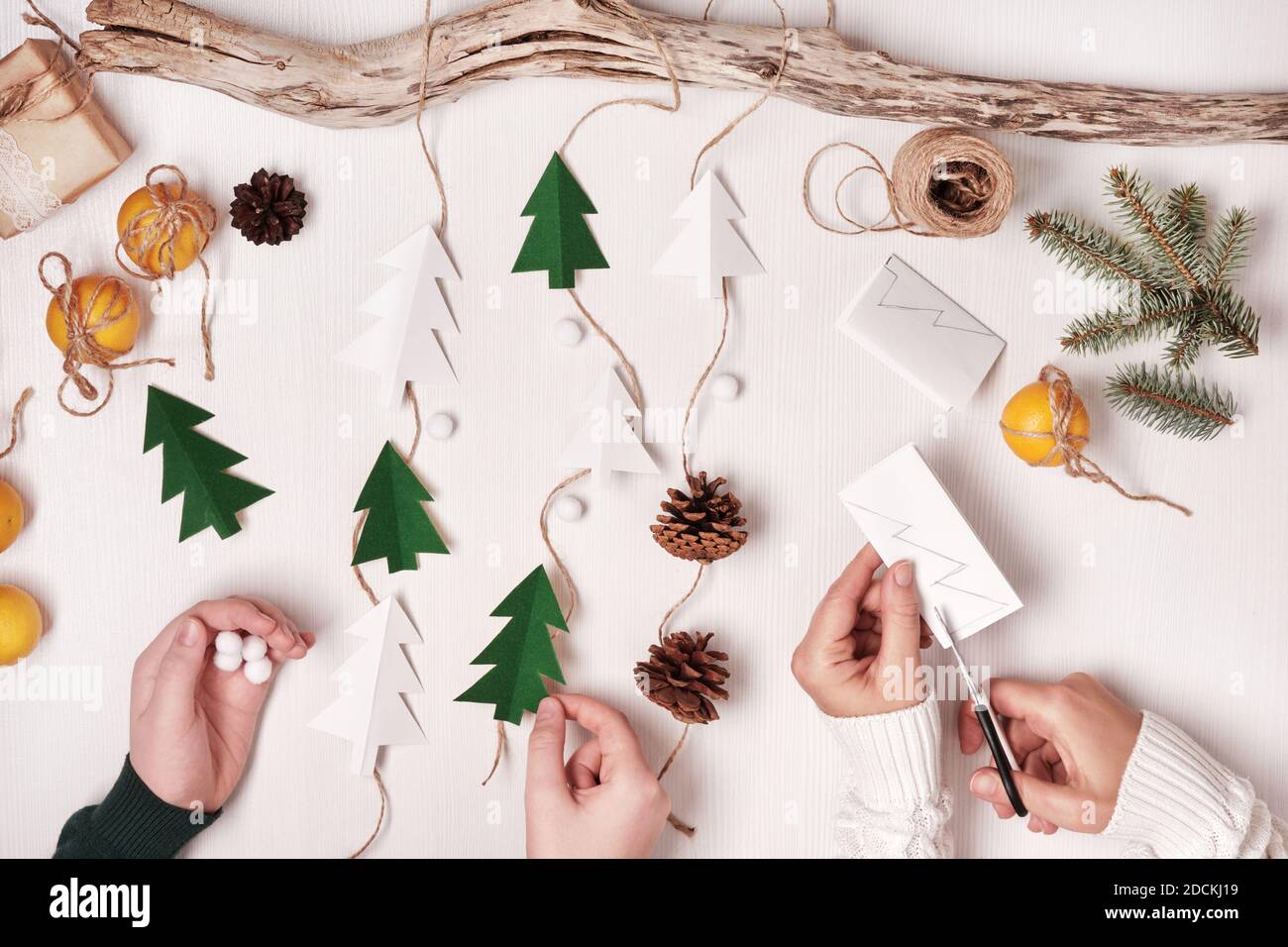 DIY decoración casera de Navidad de materiales naturales. Las manos hacen  guirnalda de árboles de papel, cordel y conos Fotografía de stock - Alamy