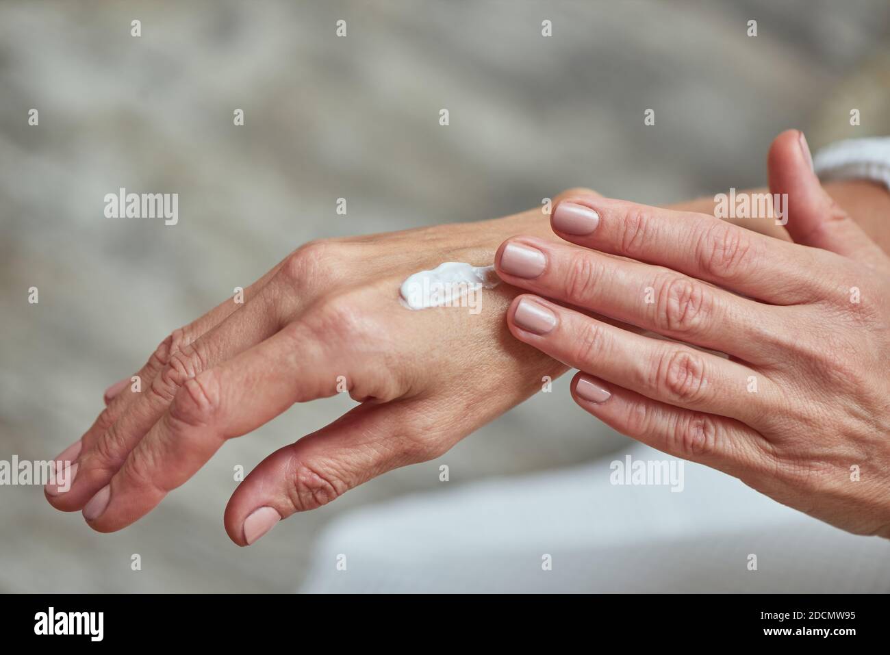 Primer plano de hermosas manos femeninas aplicando crema blanca sobre fondo claro. Concepto de belleza, cuidado de la piel y cosmetología Foto de stock