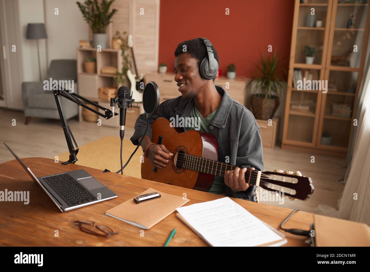 Retrato de un hombre afroamericano sonriente cantando al micrófono y tocando la guitarra mientras grababa música en el estudio, espacio de copiado Foto de stock