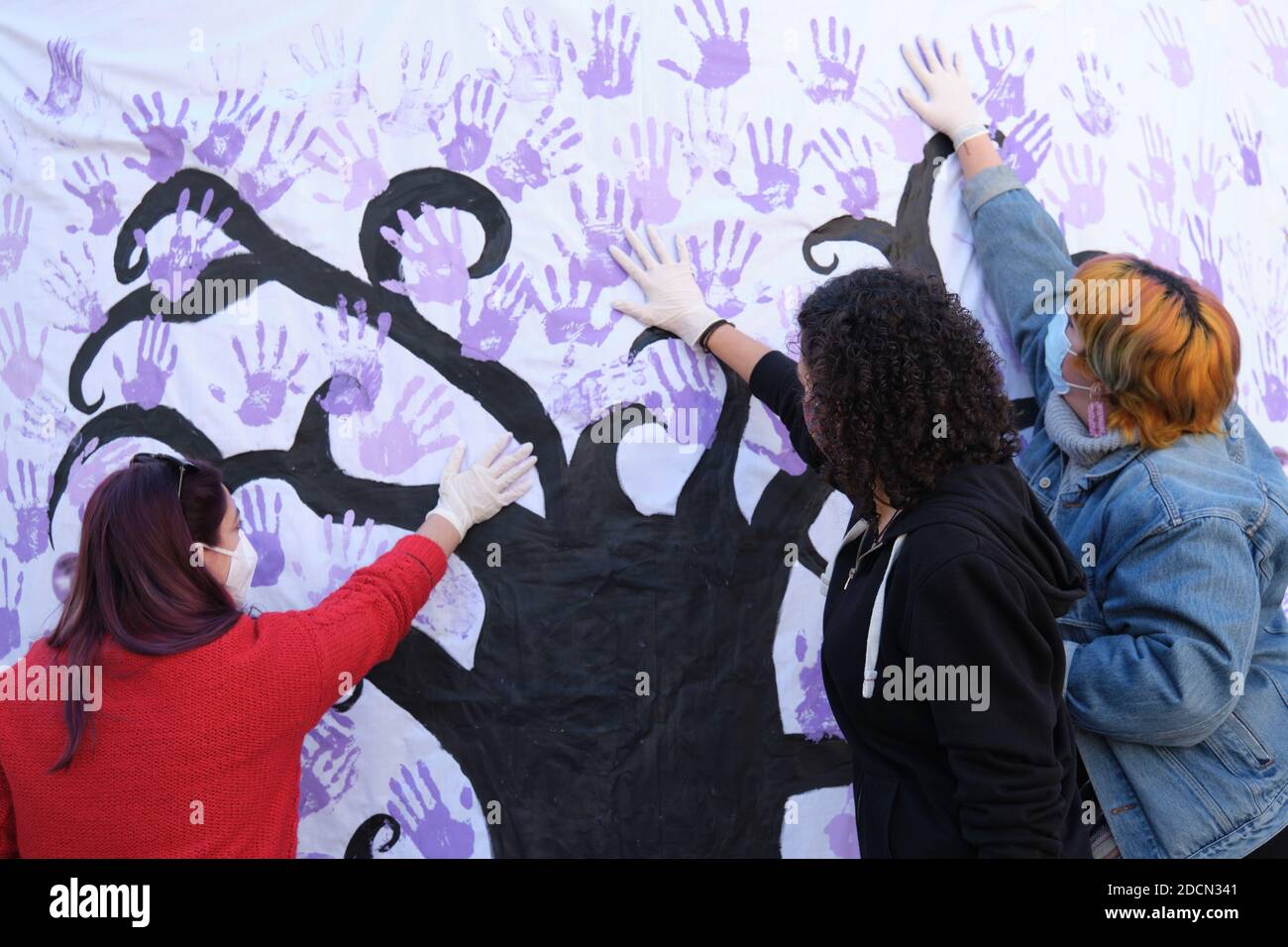 Tres mujeres participan en el mural participativo del día Internacional para la Eliminación de la violencia contra la Mujer. 25 de noviembre. Foto de stock
