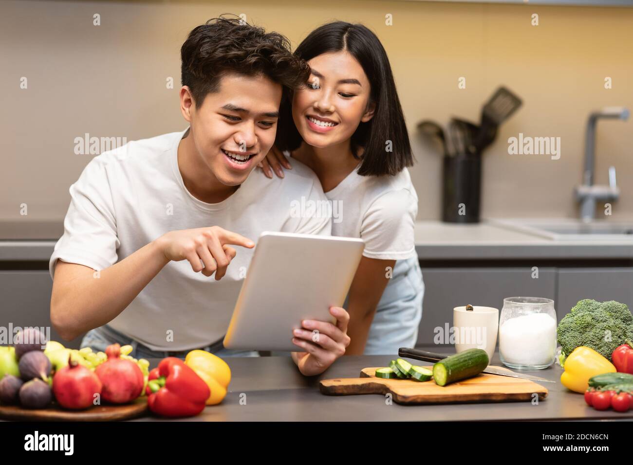 Marido y mujer coreanos cocinando usando una tableta digital en la cocina Foto de stock