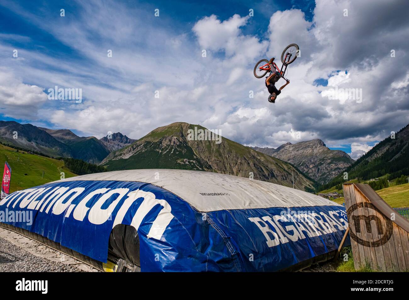 Un ciclista de descenso está practicando un salto difícil con la seguridad de aterrizar en un gran airbag en el Mottolino Bike Park, que rodea las montañas de Livi Foto de stock