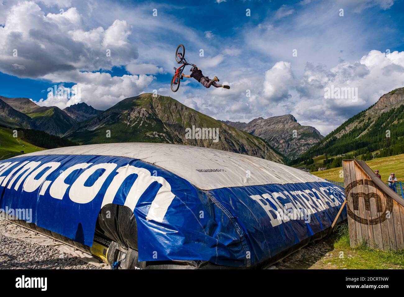Un ciclista de descenso está practicando un salto difícil con la seguridad de aterrizar en un gran airbag en el Mottolino Bike Park, que rodea las montañas de Livi Foto de stock