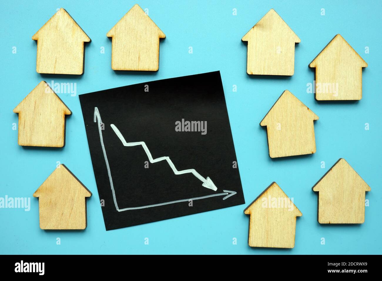 Concepto de descenso de los precios de los bienes raíces. Flecha abajo y casas de madera. Foto de stock