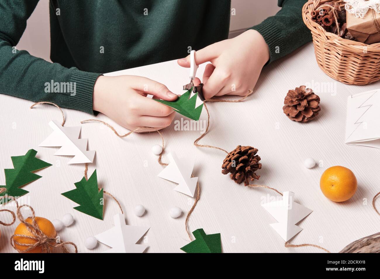 DIY decoración casera de Navidad de materiales naturales. Las manos hacen  guirnalda de árboles de papel, cordel y conos Fotografía de stock - Alamy