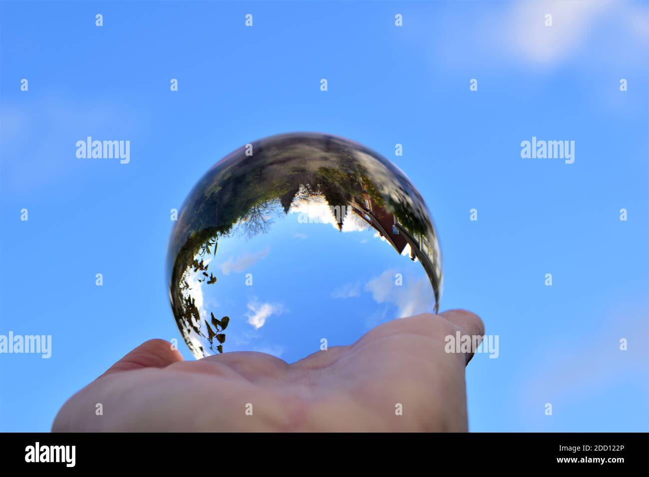 Cielo azul y algunos árboles a través de una bola de cristal por un lado humano Foto de stock