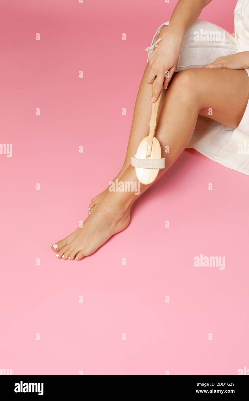 de cerca, chica haciendo un masaje de pies anticelulitis seco con un cepillo de madera sobre un fondo rosa Foto de stock