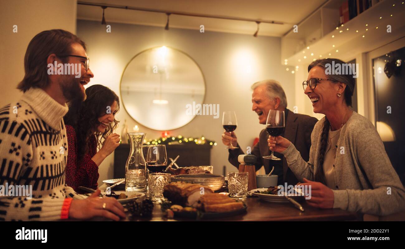Feliz familia sentada en la mesa de la cena hablando y bebiendo vino tinto. Familia cenando de Navidad en casa. Foto de stock