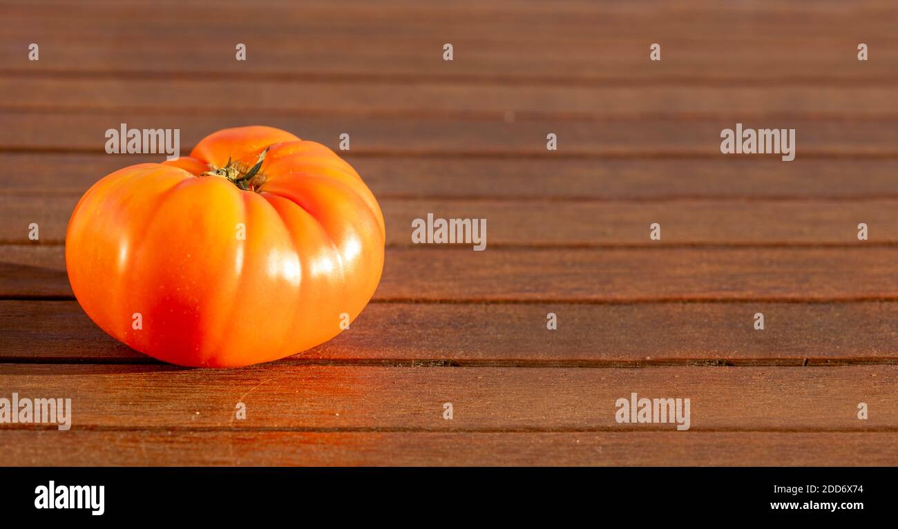 Un solo tomate de pueblo maduro rojo. Fondo de comida natural sobre madera marrón con espacio de copia. Luz solar que se refleja en la fruta. Foto de stock