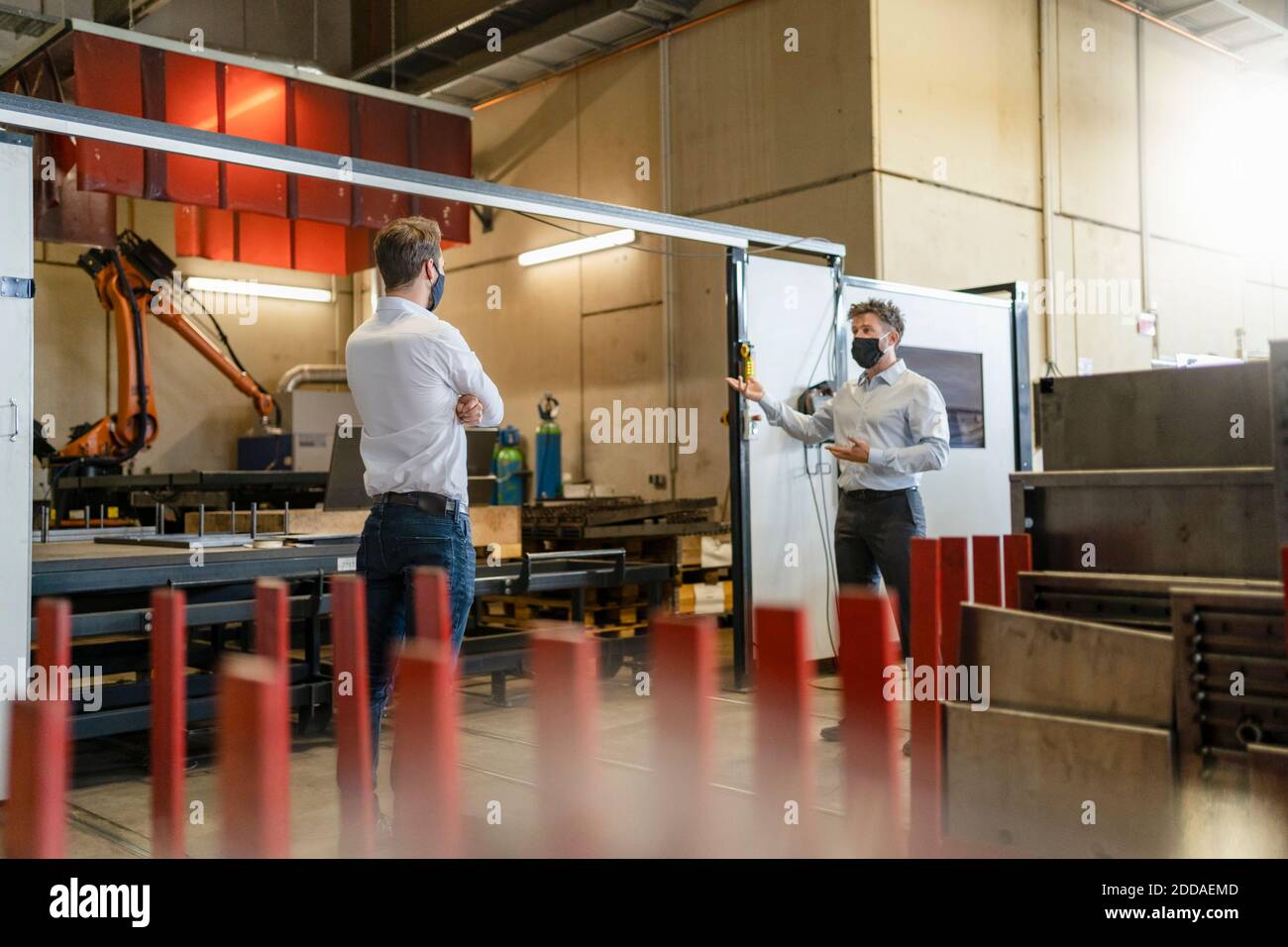 Hombres de negocios con máscara de pie con distancia social mientras trabajan en la fábrica Foto de stock
