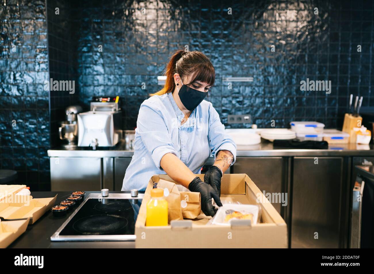 La chef lleva mascarilla mientras mantiene la comida para llevar en caja de  cartón en el mostrador de la cocina del restaurante Fotografía de stock -  Alamy