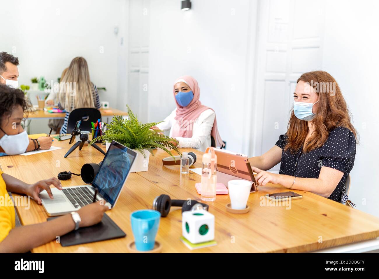 Los empleados que usan máscara para la cara sentados a distancia social mientras trabajan en la oficina Foto de stock