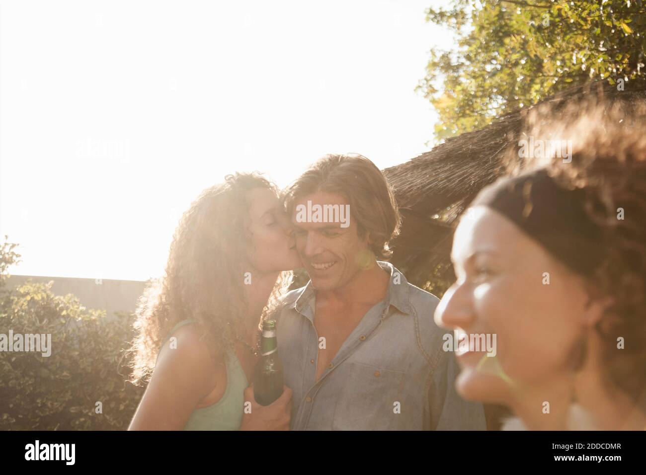 Una mujer cariñosa besando a su novio mientras disfruta de una fiesta de verano contra el cielo Foto de stock