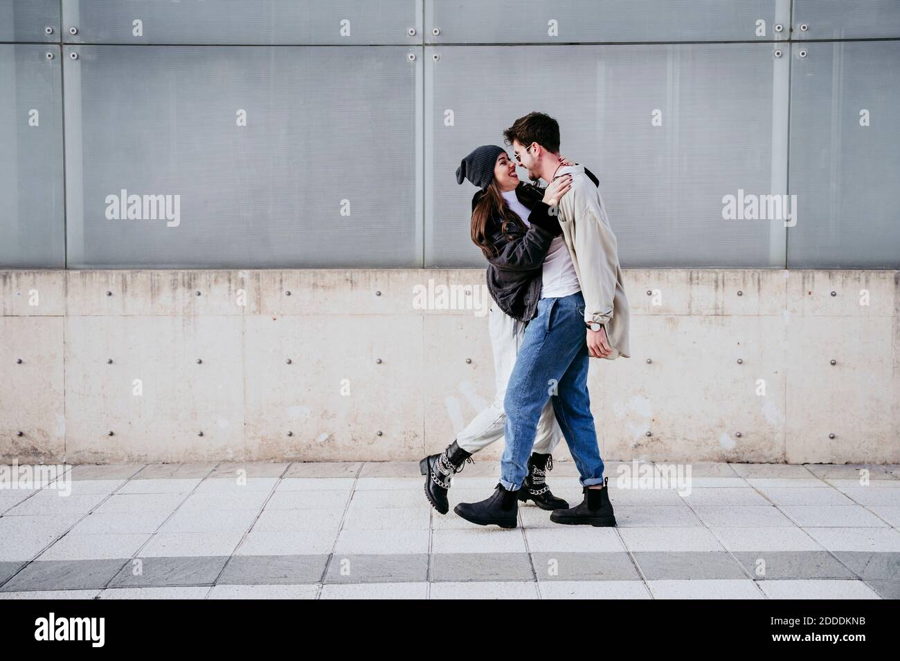 Mujer sonriente abrazando a su pareja mientras está de pie contra la pared Foto de stock