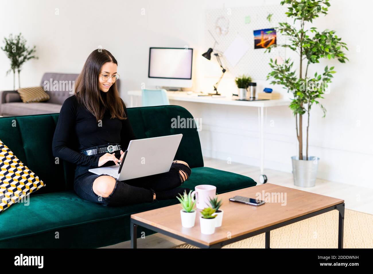 Sonriente hermosa mujer joven utilizando el portátil para blogging mientras se sienta en el sofá de casa Foto de stock