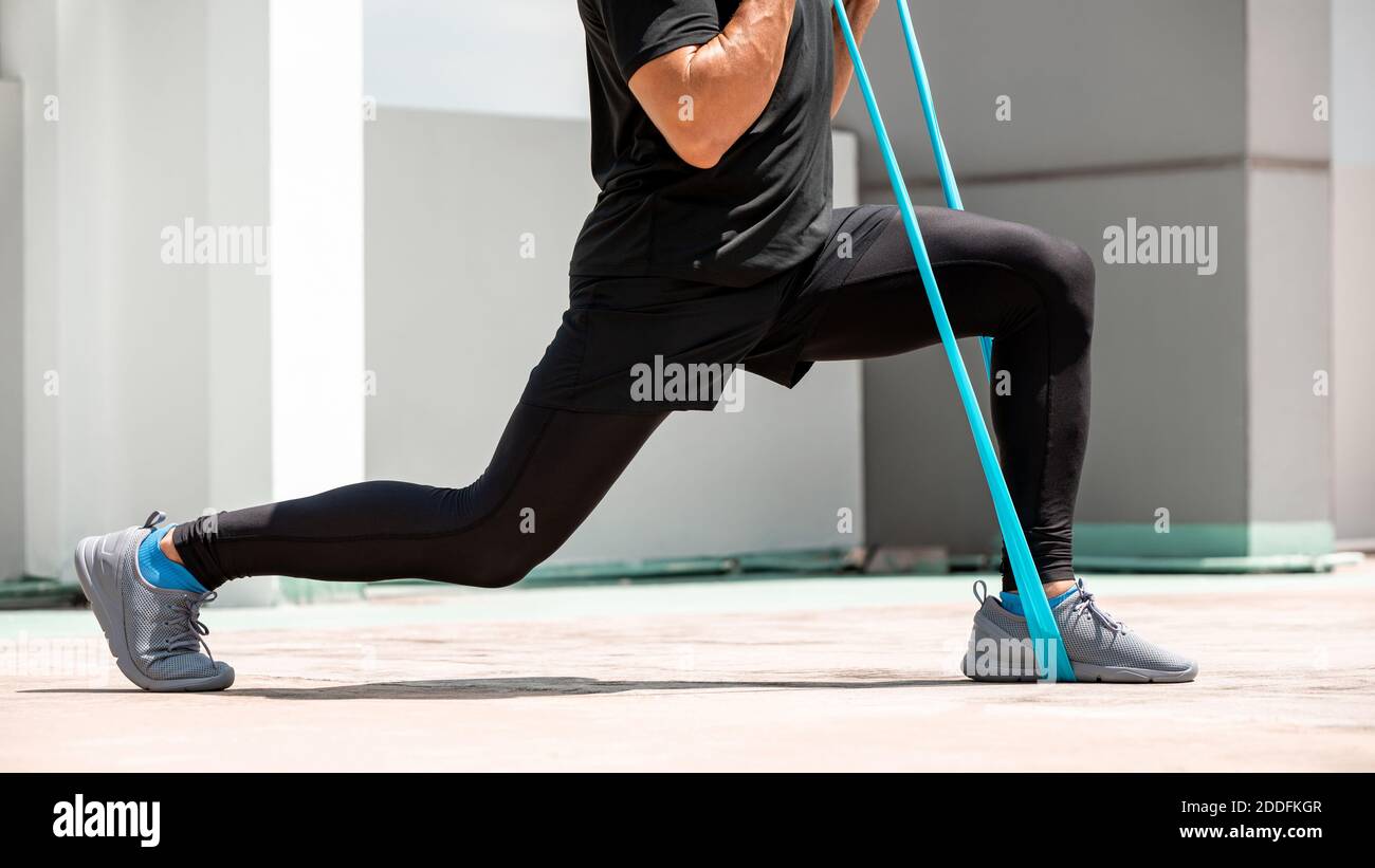 Parte inferior de un hombre haciendo ejercicio de lunge con banda de resistencia al aire libre en el sol, ejercicio en casa en el concepto al aire libre Foto de stock