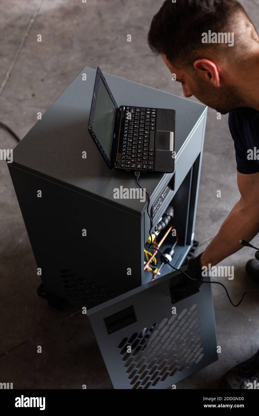 Hombre adulto en el uso de la computadora portátil para programar la  máquina rota durante trabajar en un taller moderno Fotografía de stock -  Alamy