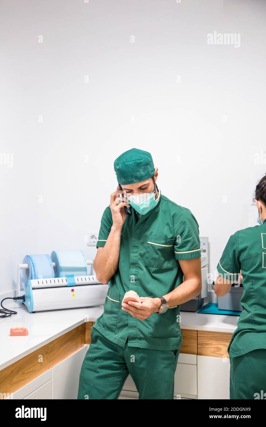 Dentista masculino en máscara y uniforme hablando en smartphone mientras la  celebración de un elenco dental en un hospital dental moderno Fotografía de  stock - Alamy