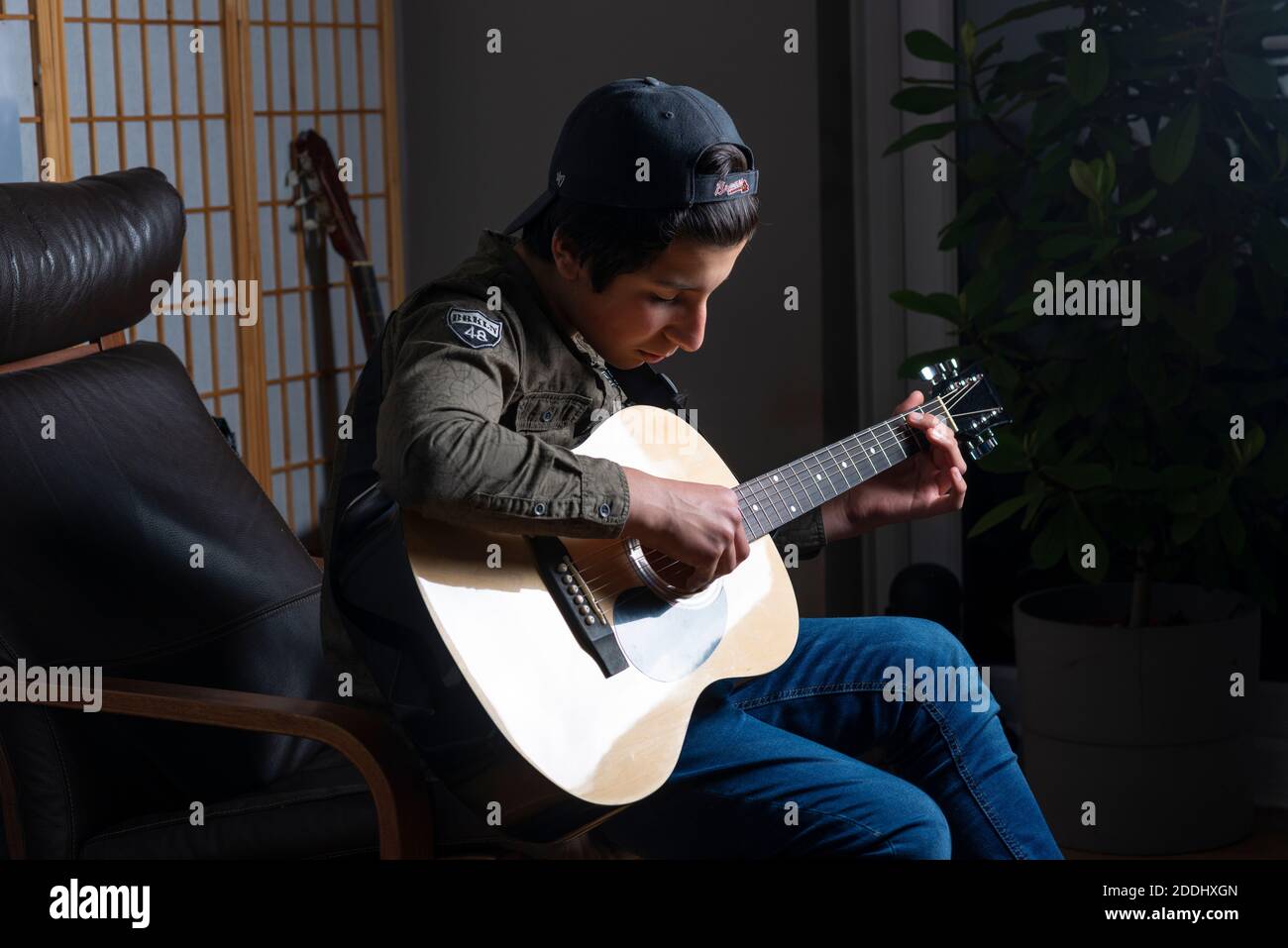Adolescente, de 14 años, toca una guitarra acústica en casa, Reino Unido Foto de stock