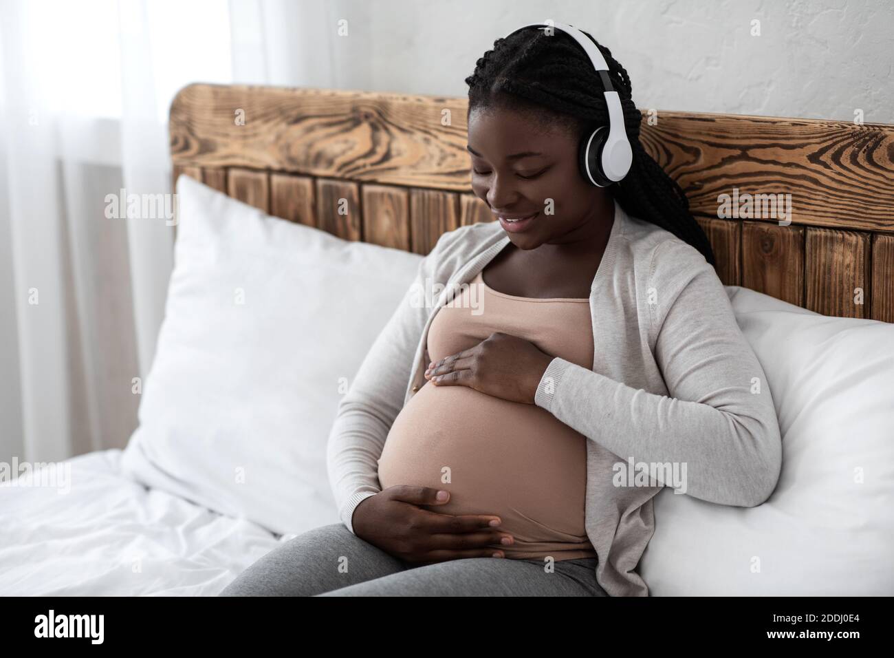 Música de embarazo. Feliz Negro embarazada Mujer en auriculares  inalámbricos relajarse en la cama Fotografía de stock - Alamy