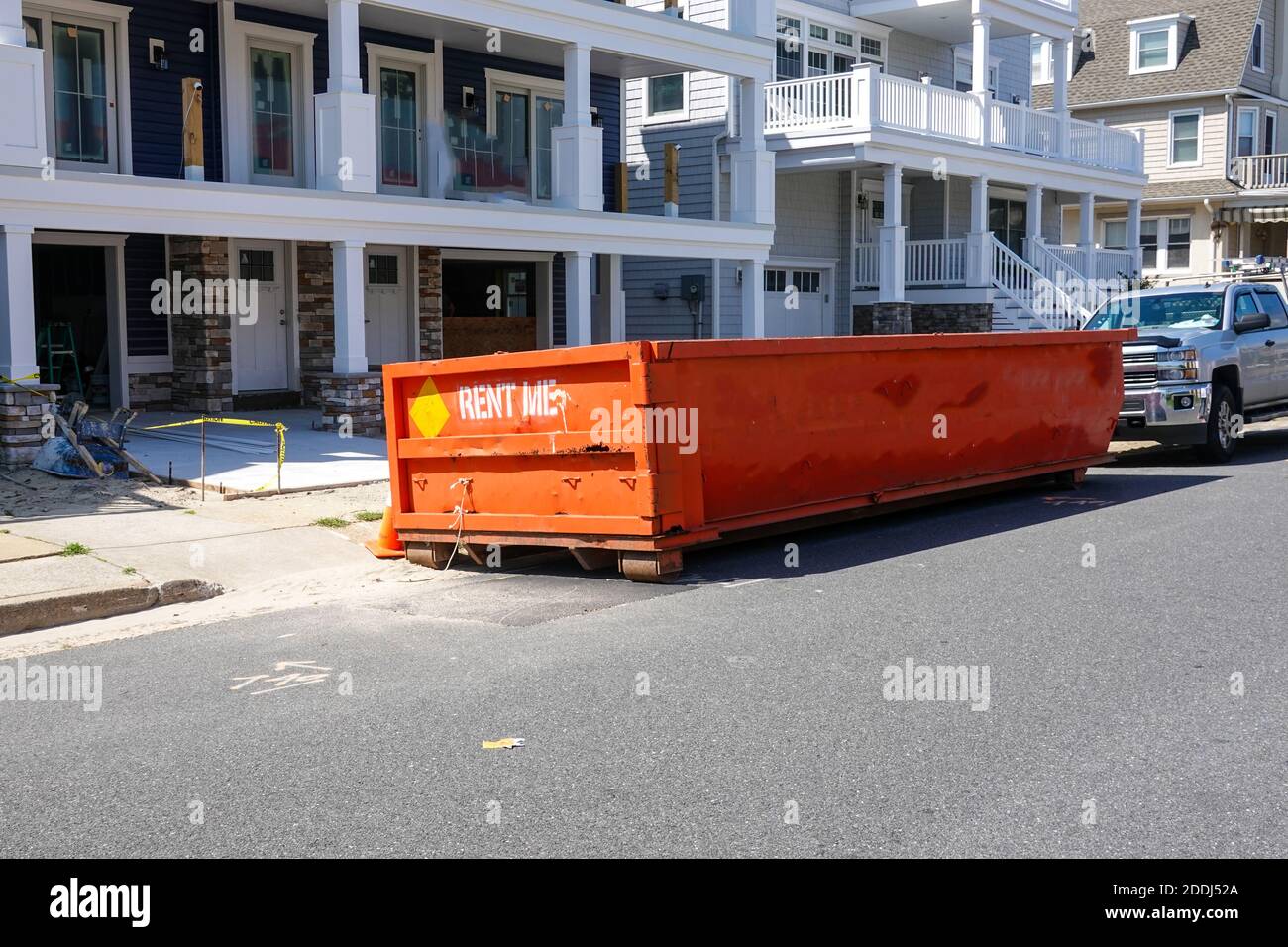 El final de un contenedor de naranja visto en una calle delante de un camión en un sitio de construcción en un día soleado Foto de stock