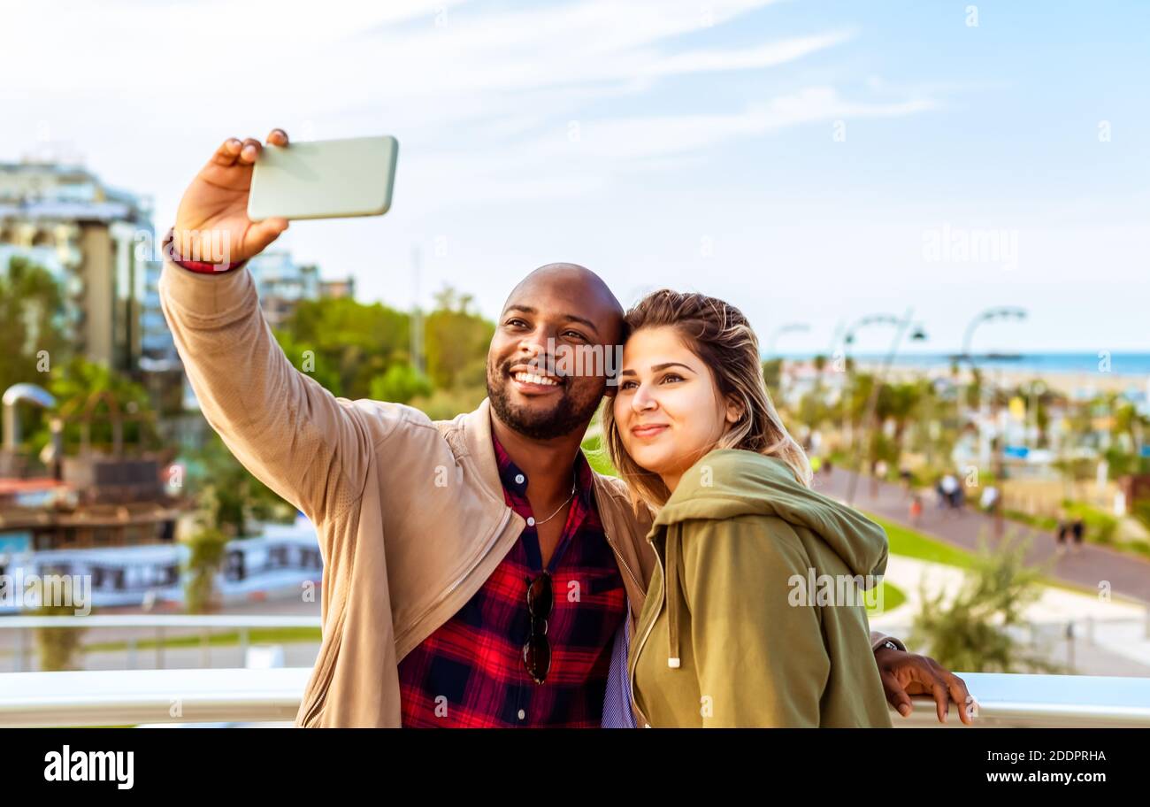joven pareja interracial de un hombre negro calvo y un mujer caucásica  tomando una foto de sí mismo en el coastline.selfie tiempo durante las  vacaciones de invierno en la playa Fotografía de
