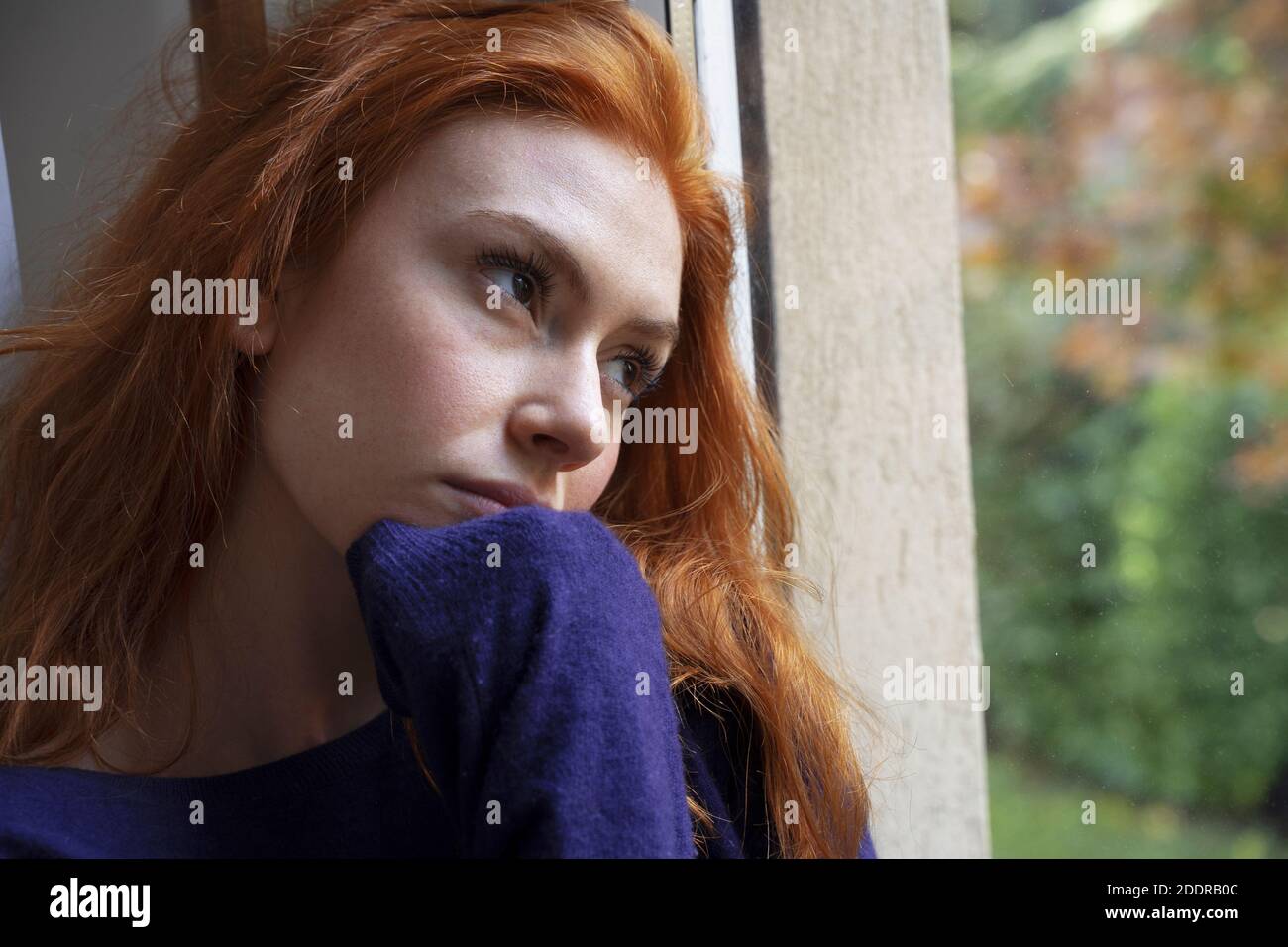 Joven mujer preocupada mirando por la ventana Foto de stock