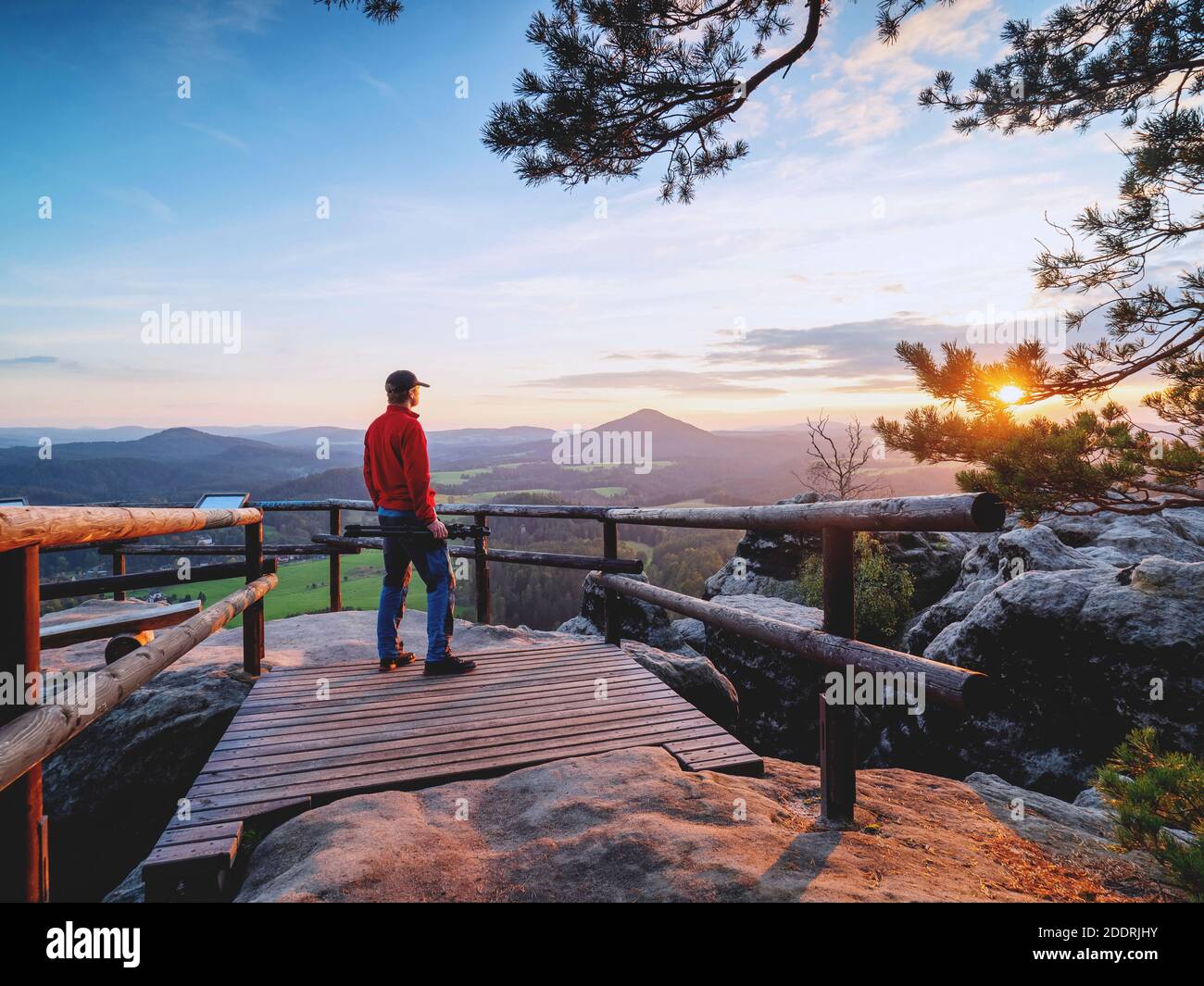 Hombre de excursionistas con trípode folden a mano ver el amanecer en el horizonte montañoso. Increíble paisaje montañoso Foto de stock